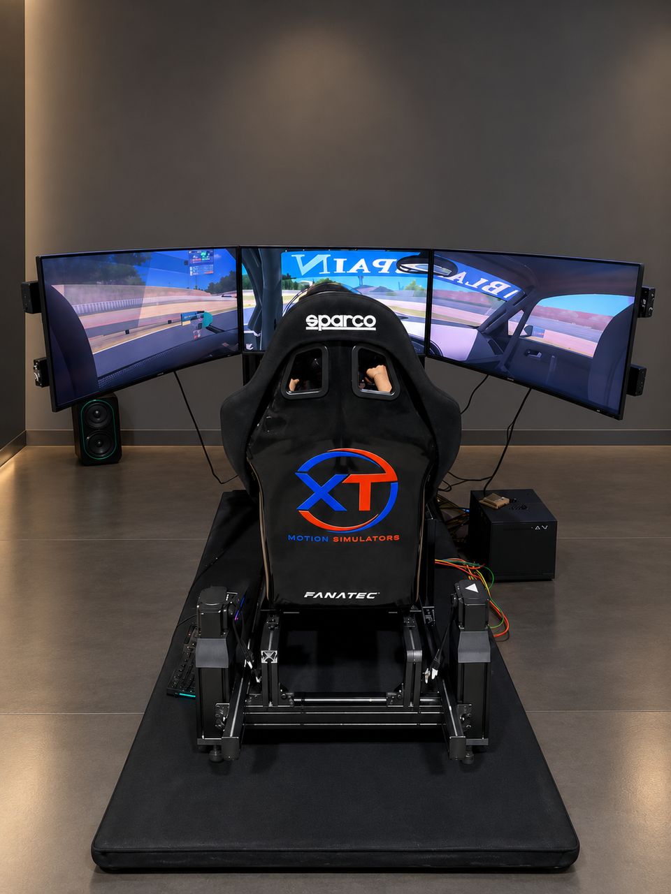 Vista trasera del simulador XT Motion: asiento tipo bucket Sparco con el logo de XT Motion, plataforma de movimiento con actuadores, chasis de perfil de aluminio y triple monitor curvo